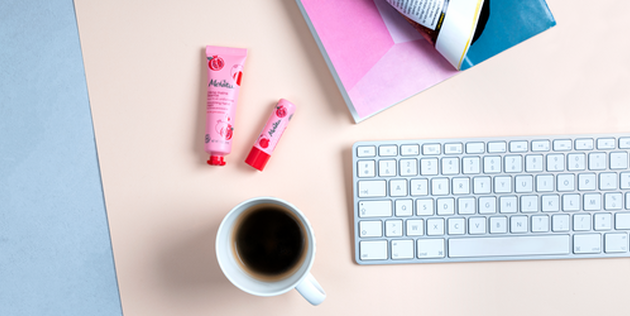 vue de haut d'un bureau o&ugrave; sont dispos&eacute;s un duo de soins mains & l&egrave;vres, un clavier et une tasse de caf&eacute;