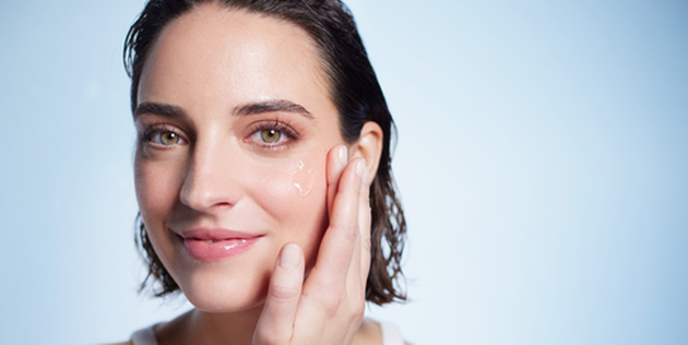 femme se touchant le visage avec la main sur fond bleu clair