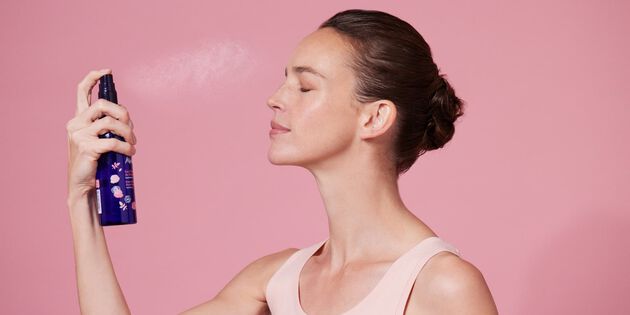 Une femme vaporise son visage avec de l'eau florale de rose ancienne