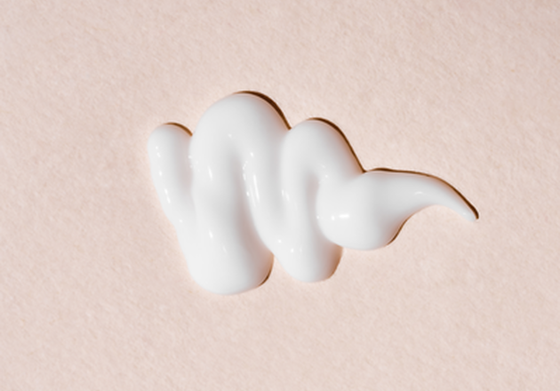 Zoom sur la texture d'une cr&egrave;me blanche sur un fond rose clair