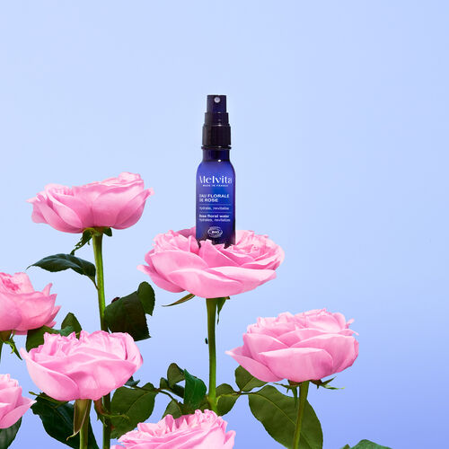 Agrandir la vue3/8 de L'eau florale de rose 50ml est pos&eacute;e sur une rose avec plusieurs roses &eacute;galement en dessous sur un fond bleur clair