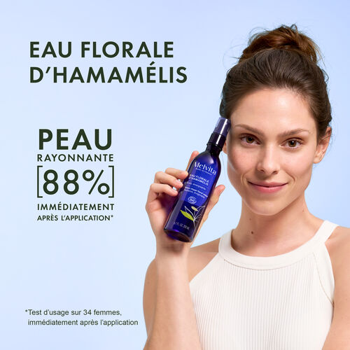 Agrandir la vue2/10 de Une femme pose avec sa main la bouteille contre sa tempe. A gauche "EAU FLORALE D'HAMAMELIS", en dessous "PEAU RAYONNANTE 88% imm&eacute;diatement apr&egrave;s l'application*". En bas "*Test d'usage sur 34 femmes, imm&eacute;diatement apr&egrave;s l'application"